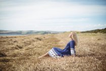 Side view of attractive blonde woman sitting in field — Stock Photo