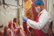 Macellaio appeso carne rossa nel ripostiglio in macelleria — Foto stock