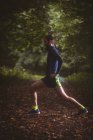 Atleta realizando exercício de alongamento na floresta — Fotografia de Stock