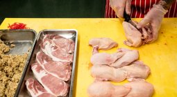 Mãos de açougueiro cortando frango no balcão de trabalho no açougue — Fotografia de Stock