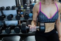 Mi-section de femme soulevant haltères à la salle de gym — Photo de stock