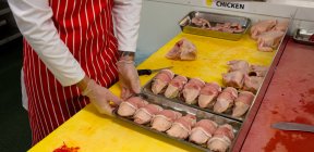 Sección media del carnicero sosteniendo bandejas de pollo y filetes en la carnicería - foto de stock