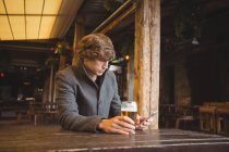 Homem usando telefone celular enquanto toma um copo de cerveja no bar — Fotografia de Stock