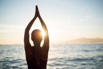 Вид ззаду жінки, що практикує йогу на пляжі під час заходу сонця — стокове фото
