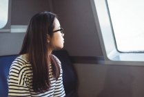 Thoughtful young woman looking through window while travelling in ship — Stock Photo