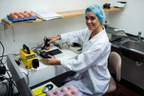 Personal femenino examinando huevo en monitor de huevo digital en fábrica de huevo - foto de stock