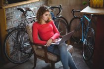 Frau sitzt auf Stuhl und benutzt Laptop in Fahrradladen — Stockfoto