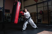 Vista laterale di Donna che pratica karate con sacco da boxe in palestra — Foto stock