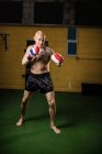 Boxer tailandese tatuato senza maglietta che pratica la boxe in palestra — Foto stock