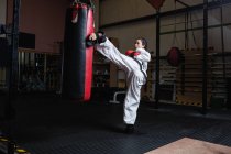 Atletica Donna pratica karate con sacco da boxe in palestra — Foto stock