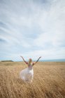Back view of blonde woman standing in field with open arms — Stock Photo