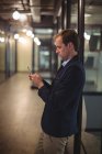 Бизнесмен печатает сообщение на мобильном телефоне в коридоре в офисе — стоковое фото