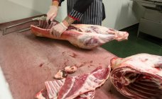 Sección media del carnicero cortando las costillas de la canal de cerdo en la carnicería - foto de stock
