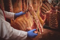 Mani di macellaio appeso carne rossa in magazzino presso macelleria — Foto stock