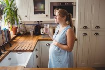 Vue latérale de l'eau potable femme enceinte dans la cuisine à la maison — Photo de stock