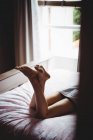 Las piernas de la mujer acostada en la cama en el dormitorio en casa - foto de stock