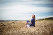 Усміхнена приваблива блондинка сидить у полі — стокове фото