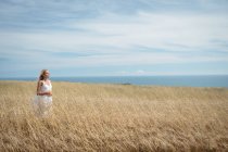Безтурботна блондинка в білій сукні, що стоїть у полі — стокове фото