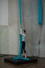 Gymnaste tenant une corde en tissu bleu sur un tapis d'atterrissage dans un studio de fitness — Photo de stock
