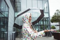 Vista lateral de feliz hermosa mujer sosteniendo paraguas durante la temporada de lluvias - foto de stock