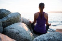 Rückansicht einer Frau, die an sonnigen Tagen Yoga auf einem Felsen praktiziert — Stockfoto