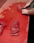 Manos de carnicero picando carne roja en la carnicería - foto de stock