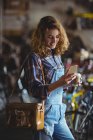 Mecânico usando telefone celular enquanto toma café na loja de bicicletas — Fotografia de Stock