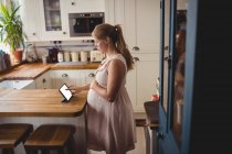Vista lateral da mulher grávida usando tablet digital na cozinha em casa — Fotografia de Stock