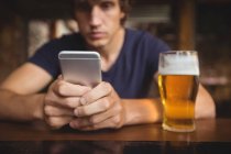 Чоловік використовує мобільний телефон з пивним склом на столі в барі — стокове фото
