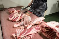 Мясник режет рёбра туши свинины в мясной лавке — стоковое фото