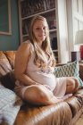 Retrato de mujer embarazada relajándose en la sala de estar en casa y mirando a la cámara - foto de stock
