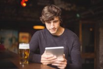 Homem com copo de cerveja usando tablet digital no balcão no bar — Fotografia de Stock