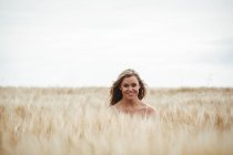 Retrato de mulher sorridente em pé no campo de trigo no dia ensolarado — Fotografia de Stock