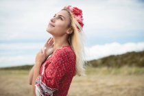 Беззаботная блондинка в цветочной тиаре стоит в поле и смотрит вверх — стоковое фото
