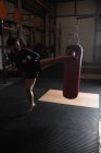 Vue grand angle du boxeur pratiquant la boxe avec sac de boxe dans le studio de fitness — Photo de stock