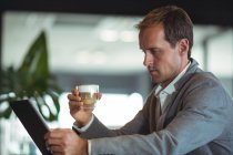 Бизнесмен пьет кофе во время работы над цифровым планшетом в кафе — стоковое фото