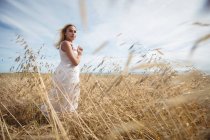 Selective focus of blonde woman standing in field and looking at camera — Stock Photo