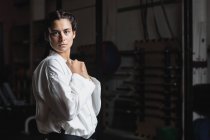 Portrait of woman in karate kimono standing in fitness studio and looking at camera — Stock Photo