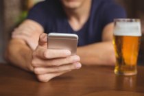 Uomo che utilizza il telefono cellulare con bicchiere di birra sul tavolo nel bar — Foto stock
