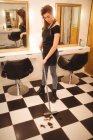 Женский парикмахер убирает волосы на полу с метлой в салуне — стоковое фото
