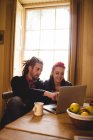 Felice coppia hipster utilizzando il computer portatile mentre seduto a tavola — Foto stock