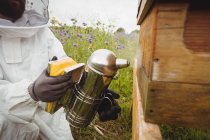 Immagine ritagliata di apicoltore utilizzando ape fumatore in campo — Foto stock