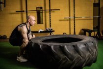 Vue latérale du beau sportif soulevant des pneus lourds dans la salle de gym — Photo de stock