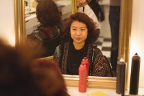 Donna sorridente seduta davanti allo specchio nel salone di parrucchiere — Foto stock
