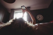 Mujer tomando selfie en el teléfono móvil en el dormitorio en casa - foto de stock