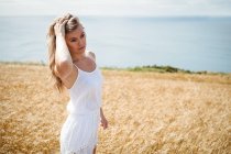 Жінка з рукою в волоссі, стоячи в пшеничному полі в сонячний день — стокове фото
