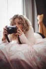Femme regardant appareil photo numérique dans la chambre à coucher à la maison — Photo de stock