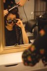Стильная женщина смотрит на солнцезащитные очки, делая прическу в профессиональной парикмахерской — стоковое фото
