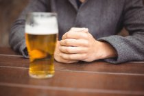Mid section of man sitting in bar with glass of beer on table — Stock Photo