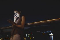 Молодая женщина разговаривает по мобильному телефону во время использования цифрового планшета — стоковое фото